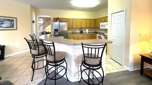 A kitchen with a central island, bar stools, wooden cabinets, a refrigerator, and a microwave. - 229 Corvina Drive Davenport, 5bed (Davenport)