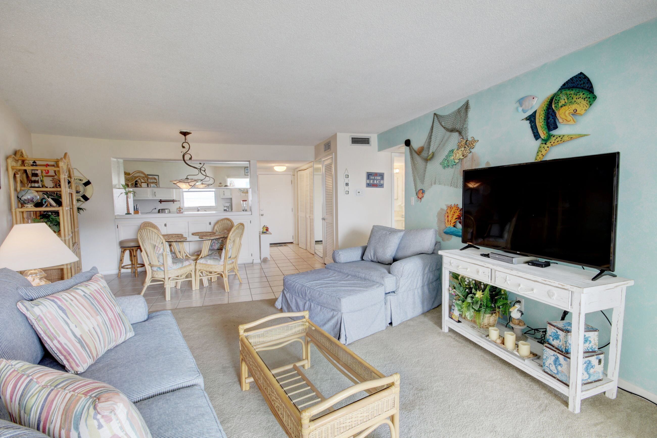 Een woonkamer met een bank, een salontafel, een televisie op een witte console en een eethoek met stoelen en een tafel.