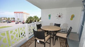 A balcony with a round table and chairs, white railings, and a view of a parking lot and buildings. - 235 El Matador (Fort Walton Beach)