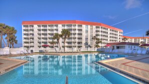 A hotel with a large pool, palm trees, and a red-roofed building. - 235 El Matador (Fort Walton Beach)