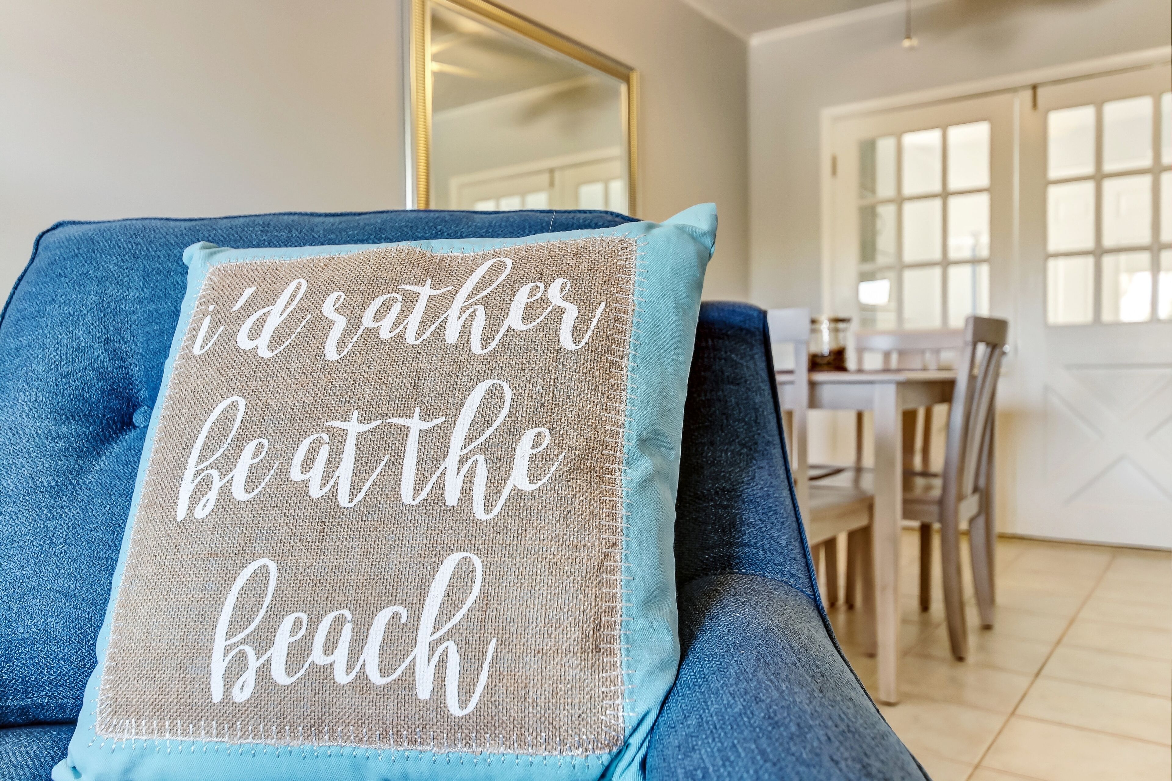 Un canapé bleu avec un coussin sur lequel on peut lire : « Je préférerais être à la plage. »