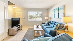A living room with a TV, sofa, coffee table, and artwork on the wall. - 2810 Ohio Avenue #1 (Fernandina Beach)