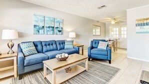 A modern living room with a blue sofa, a coffee table, and a dining area in the background. - 2810 Ohio Avenue #1 (Fernandina Beach)
