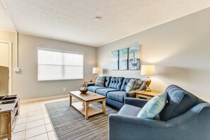 A modern living room with a sofa, armchair, coffee table, and a painting on the wall. - 2810 Ohio Avenue #1 (Fernandina Beach)