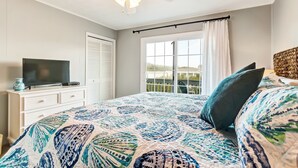 A bedroom with a bed, a television on a dresser, a window with curtains, and a ceiling fan. - 2810 Ohio Avenue #1 (Fernandina Beach)