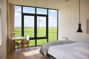 A bedroom with a large window, a bed, a desk with a chair, and a hanging light fixture.