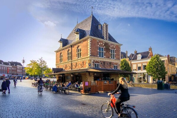 A historic building with a prominent corner entrance, a cobblestone plaza, and a cyclist in the foreground.