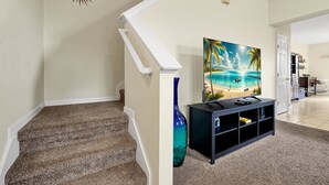 A staircase with a patterned carpet, a painting of a beach scene, and a black entertainment unit. - 2663 Andros Lane, Kissimmee, 3 BED (Kissimmee)