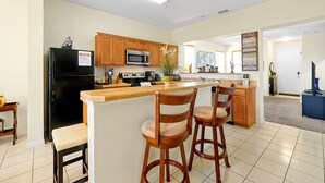 A modern kitchen with wooden cabinets, a black refrigerator, a microwave, and a large island with bar stools. - 2663 Andros Lane, Kissimmee, 3 BED (Kissimmee)