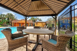 A covered outdoor seating area with wicker furniture and a pool in the background. - 2663 Andros Lane, Kissimmee, 3 BED (Kissimmee)