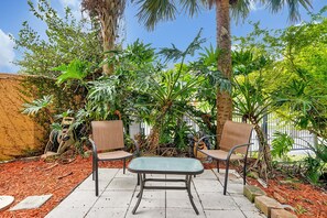 An outdoor seating area with two chairs and a table, surrounded by lush greenery and palm trees. - 2663 Andros Lane, Kissimmee, 3 BED (Kissimmee)