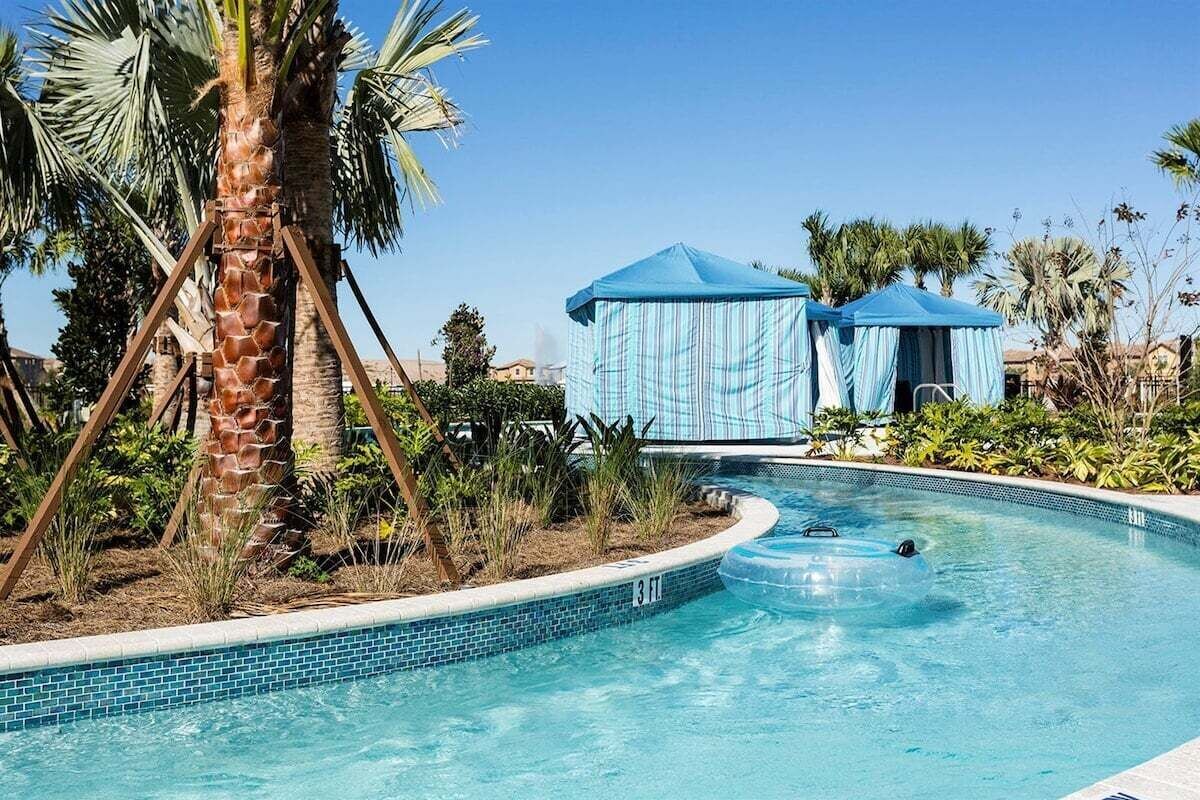 En swimmingpool med et palmetræ og et blåt telt i baggrunden.