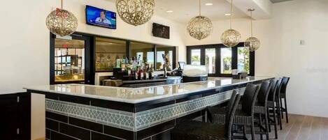 Un espace bar doté d’un long comptoir, d’un mur recouvert de carreaux noirs et blancs, et de plusieurs luminaires suspendus.