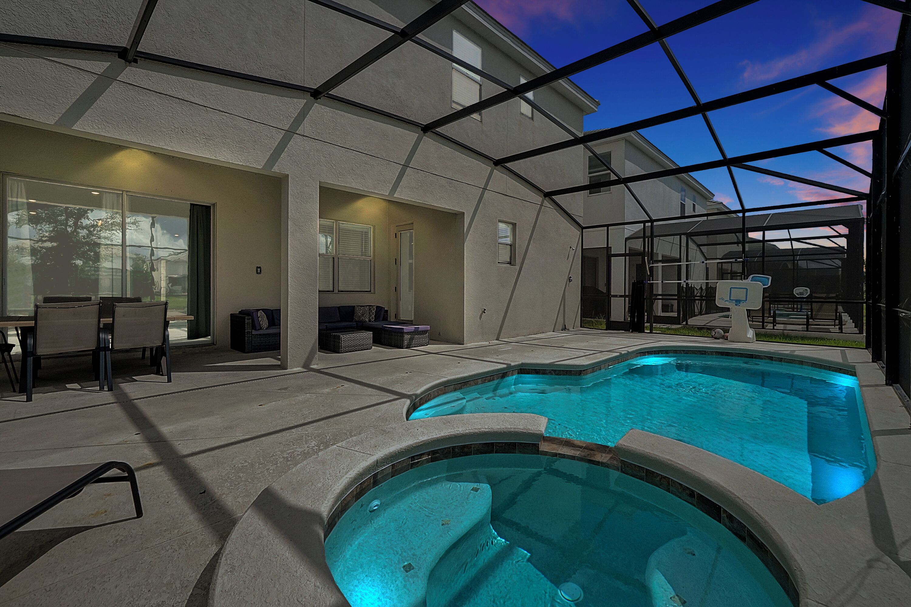 A covered outdoor swimming pool with a glass ceiling, a patio area with seating, and a view of the sky.