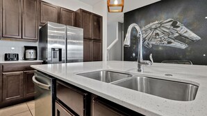 A modern kitchen with stainless steel appliances, a double sink, and a Star Wars-themed wall mural. - 2496 Shanti Drive,kissimmee,12bed (Kissimmee)