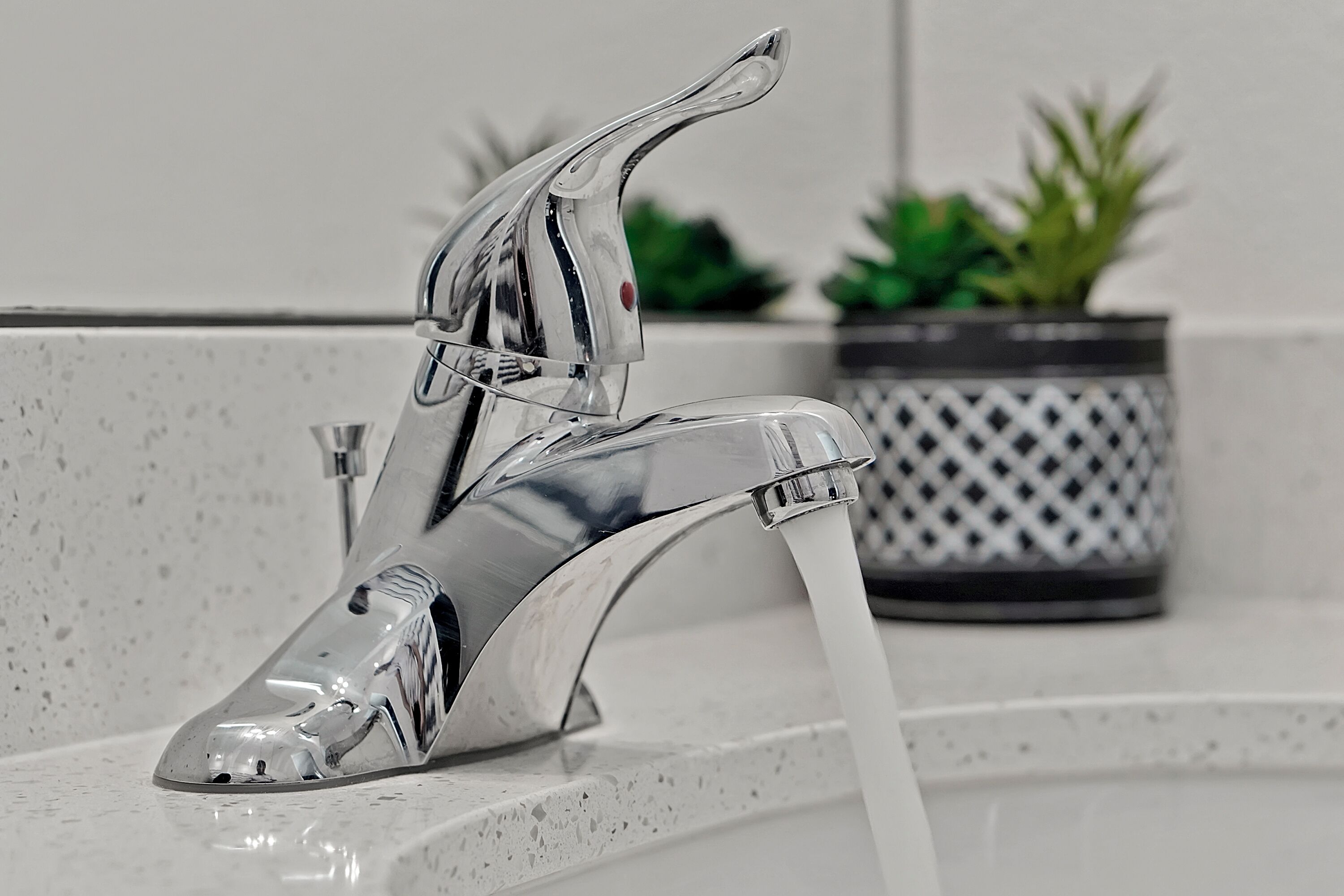 Une salle de bain moderne avec un robinet chromé et une plante en pot en arrière-plan.