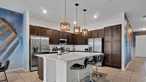 A modern kitchen with dark wooden cabinets, stainless steel appliances, a central island with bar stools, and pendant lighting. - 2496 Shanti Drive,kissimmee,12bed (Kissimmee)