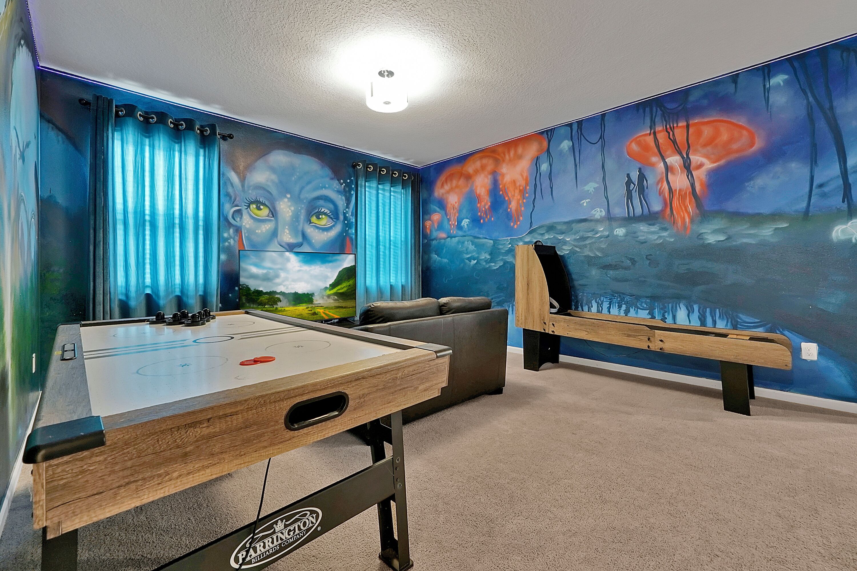 A room with a foosball table, a pool table, and a mural of a fantastical scene.