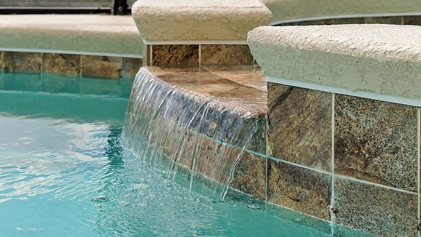 A pool with a waterfall feature, stone steps, and a clear blue water surface. - 2496 Shanti Drive,kissimmee,12bed (Kissimmee)