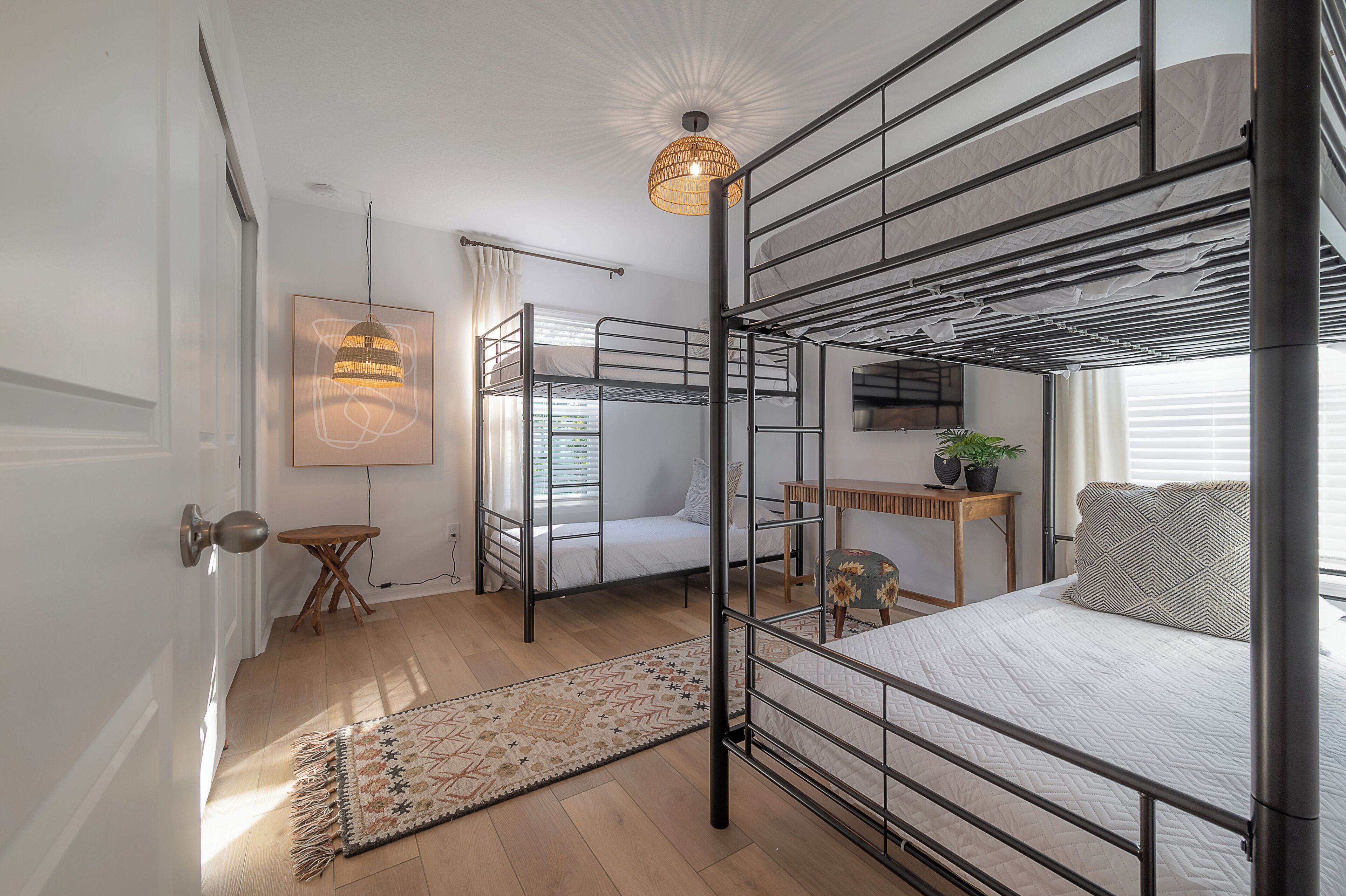 A compact, well-lit room with bunk beds, a small desk, a potted plant, and a patterned rug.