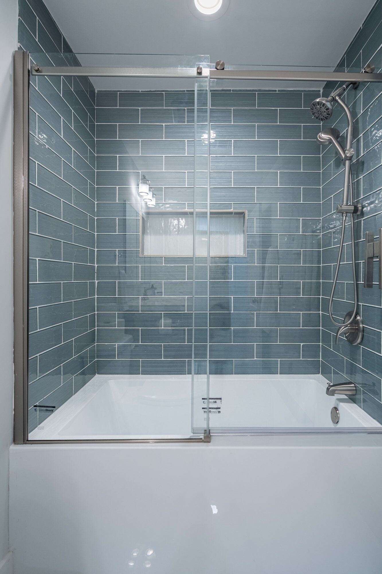 Une cabine de douche moderne dotée d’une porte en verre, d’un pommeau de douche à main et d’un robinet mural.