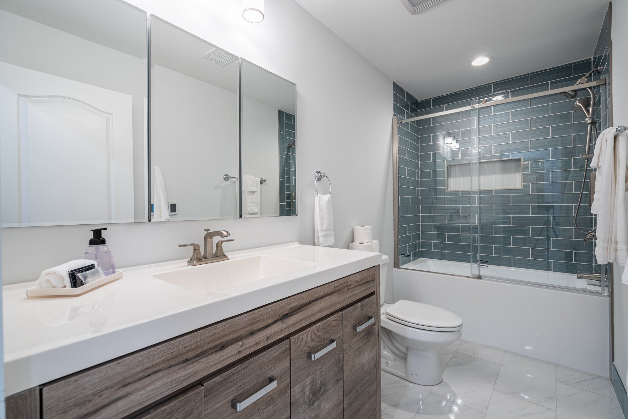 Une salle de bain moderne avec un meuble-lavabo blanc, un grand miroir, une douche aux carreaux bleus et des toilettes.
