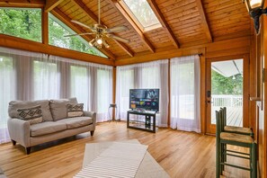A wooden-paneled room with a ceiling fan, a television on a glass stand, a sofa with cushions, and a view of a deck through a glass door. - 2431 Weatherford Court, Marietta (Marietta)