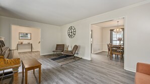A spacious living room with hardwood flooring, a dining area with a chandelier, and a large wall clock. - 2431 Weatherford Court, Marietta (Marietta)