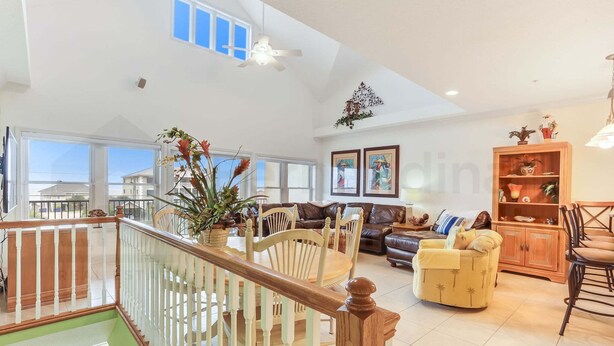 A spacious living area with a high ceiling, a staircase with wooden railings, a dining area with chairs, and a sofa. - 241 S Fletcher Ave (Fernandina Beach)