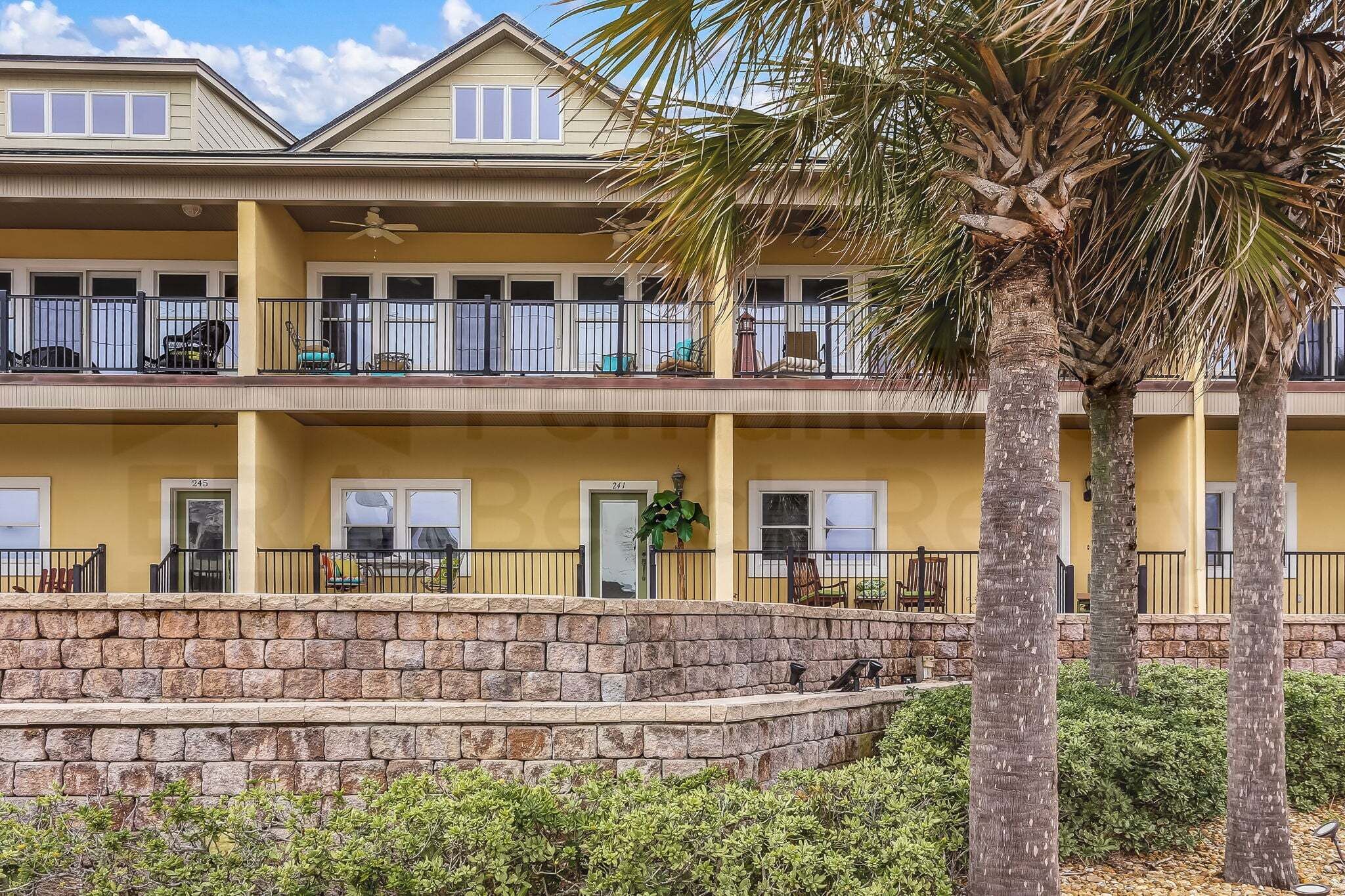 A multi-story hotel with balconies, stone steps, and palm trees.