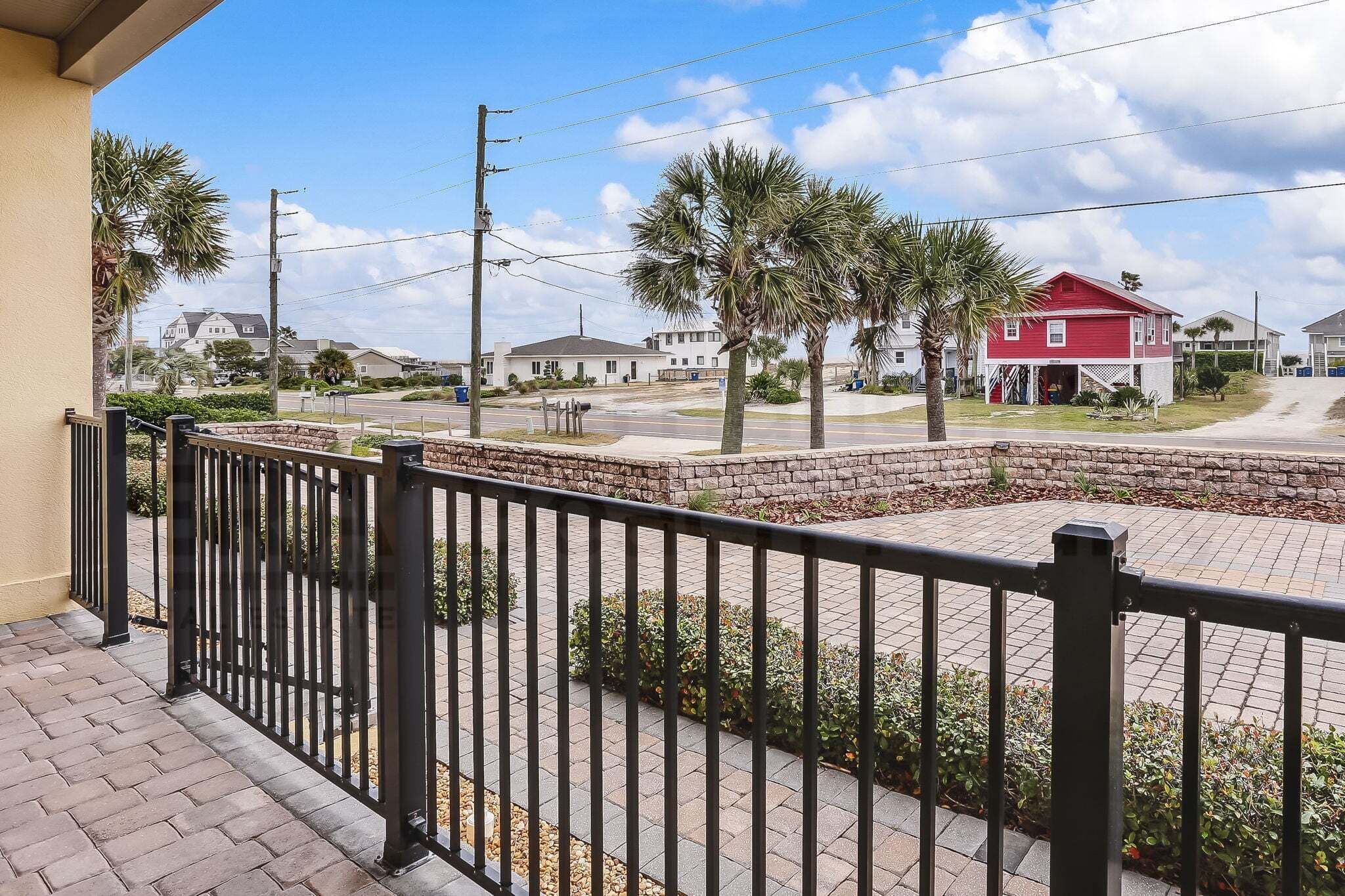 A residential area with a paved walkway, a red house, and palm trees.