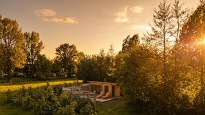 Puinen mökki, jossa on terassi ja aurinkotuoleja, ja sen ympärillä on puita ja ruohokenttä.