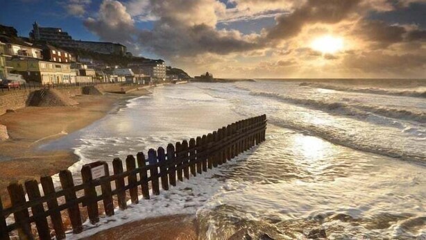 A coastal scene with a wooden sea wall, a river, and buildings along the shore. - 26 N Washington Ave (Ventnor City)