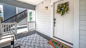 Eine Veranda mit einer Holztreppe, einer Tür mit einem Kranz und einer Fußmatte mit dem Schriftzug 'HELLO'.