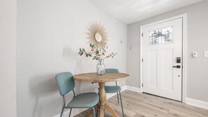 Ein Essbereich mit einem runden Holztisch, zwei blaugrünen Stühlen, einer Blumenvase und einem Wandspiegel.