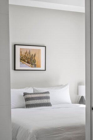 A neatly made bed with white linens and a patterned pillow, a framed picture on the wall, and a bedside table with a lamp. - 2880: Art Inspired Retreat at Espadin (Denver)