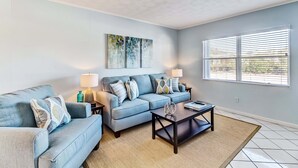 A living room with a sectional sofa, two side tables, a coffee table, and a large window with blinds.