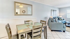 A dining area with a table and chairs, a mirror, a clock, and a sofa in a living room.