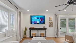 Ein Wohnzimmer mit Flachbildfernseher, Deckenventilator und Ausblick ins Freie.