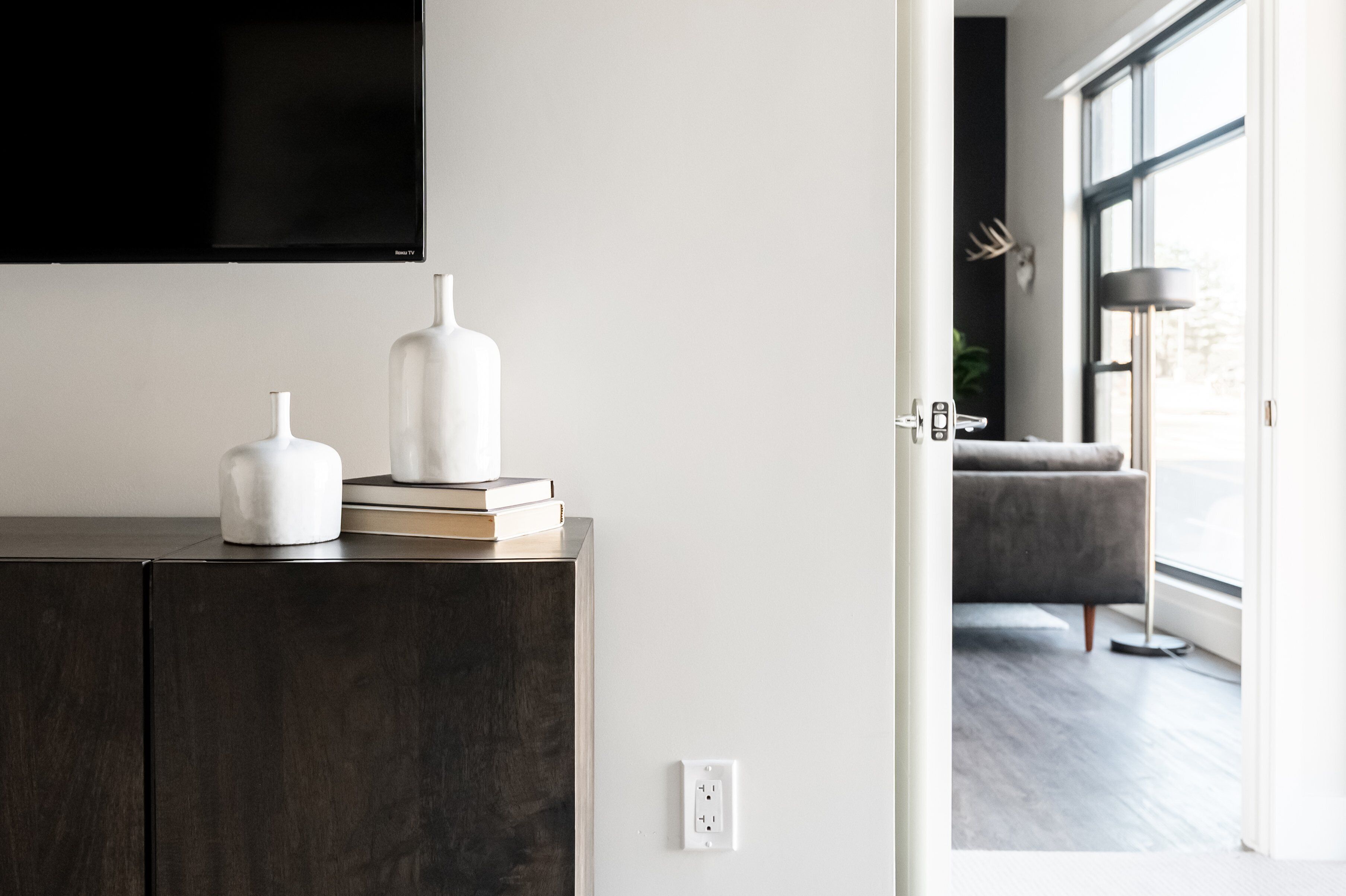 A modern living room with a dark wooden cabinet, a flat-screen TV mounted on the wall, and a grey sofa.