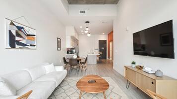 A modern living room with a white sofa, a wooden coffee table, and a TV mounted on the wall.