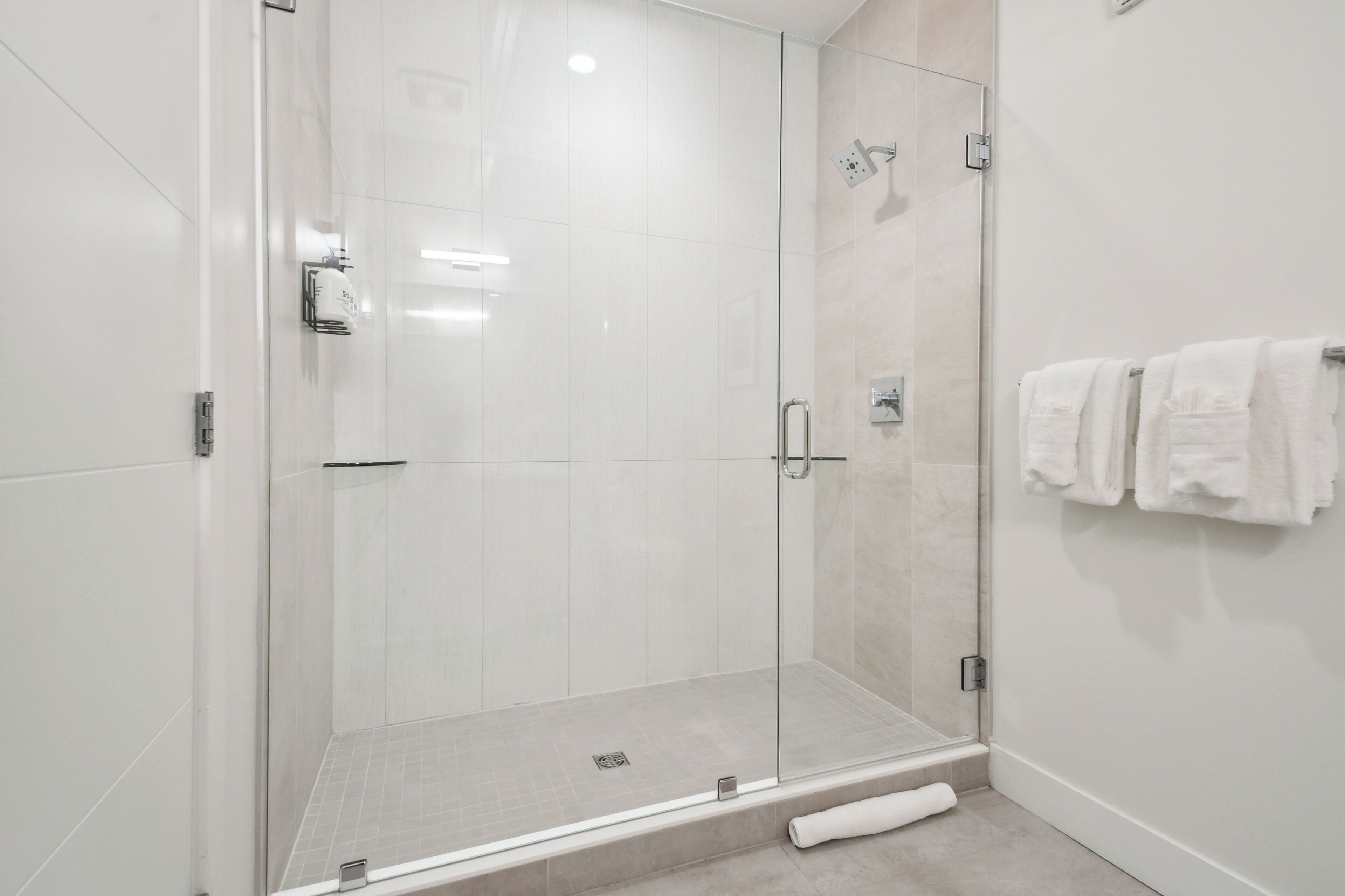 A modern bathroom with a glass shower enclosure, white tiled walls, and a towel rack with two towels.