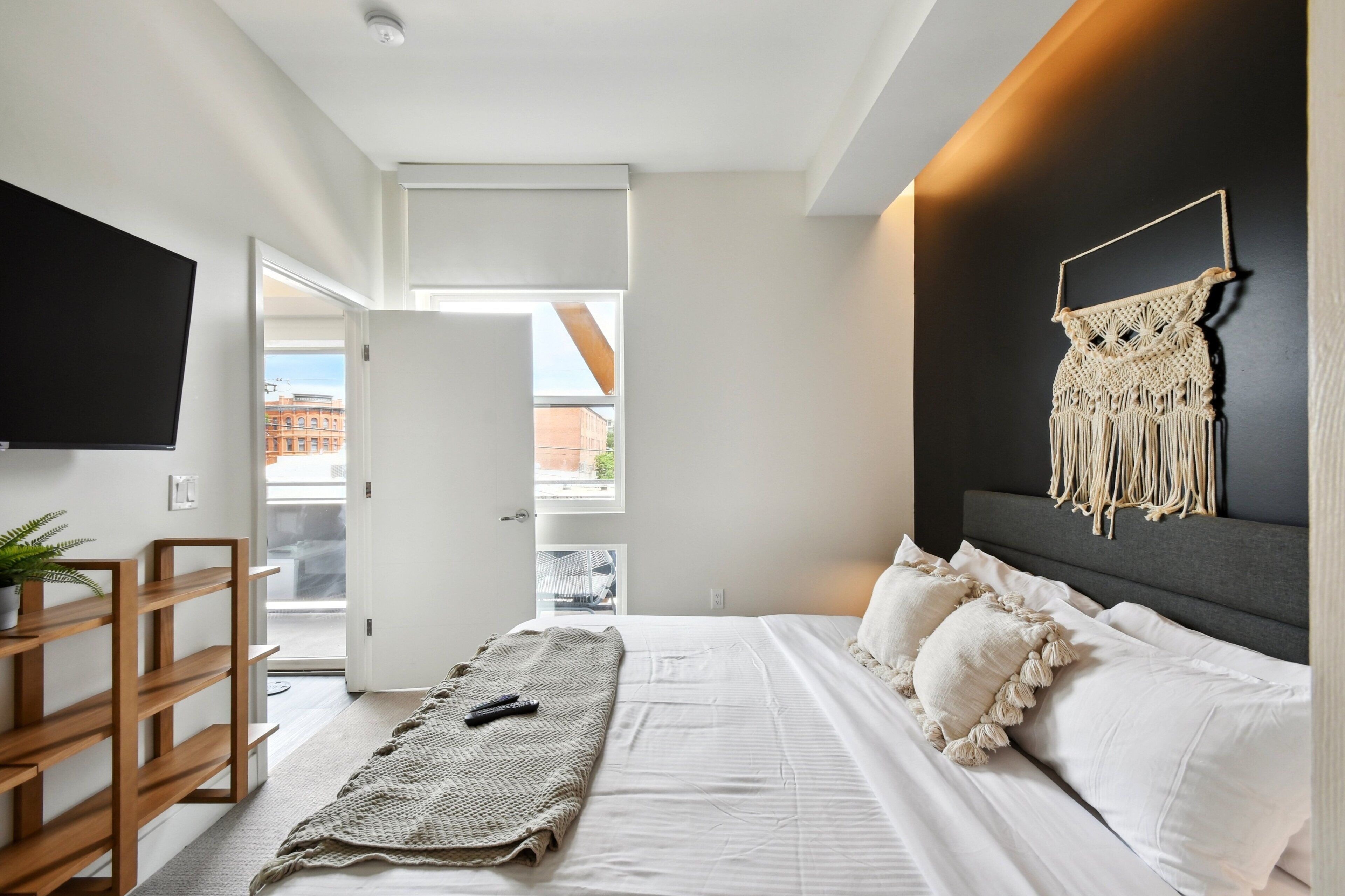 Een moderne slaapkamer met een bed, een televisie en een macramé wandversiering.
