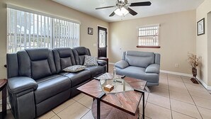 A living room with a black leather sofa, a grey armchair, a glass coffee table, and a ceiling fan. - 2737 Bel Aire Circle (Tampa)
