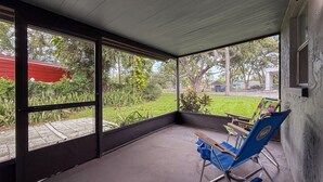 A covered outdoor area with a concrete floor, large windows, and a blue folding chair. - 2737 Bel Aire Circle (Tampa)