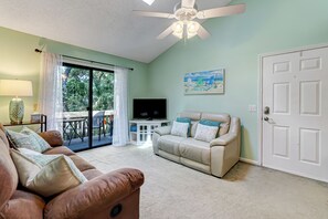 A living room with a beige sofa, a brown leather couch, a TV, and a painting on the wall. - 2745 Forest Ridge (Fernandina Beach)