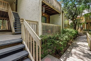 A wooden staircase leading to a balcony with a railing, surrounded by greenery and a wooden deck. - 2745 Forest Ridge (Fernandina Beach)