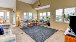 Ein geräumiges Wohnzimmer mit einem großen Deckenventilator, zwei Sofas, einem Couchtisch und einem Fernseher auf einem Holzständer.