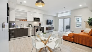 A modern kitchen with white cabinets, a dining area with a glass table and white chairs, and a living area with an orange sofa. - 2880: Natural Influence Sanctuary at Espadin (Denver)
