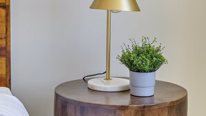Un comodino rotondo in legno con una lampada dorata e una pianta in vaso.